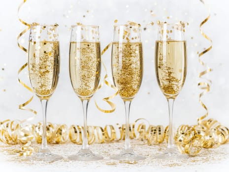Four elegant flutes filled with sparkling liquid are adorned with gold confetti. Streamers float around, enhancing the celebratory atmosphere.