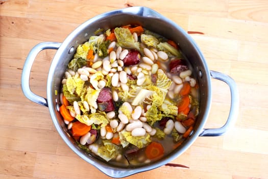 A large pot of soup with beans, carrots, and cabbage. The soup is full and has a lot of ingredients