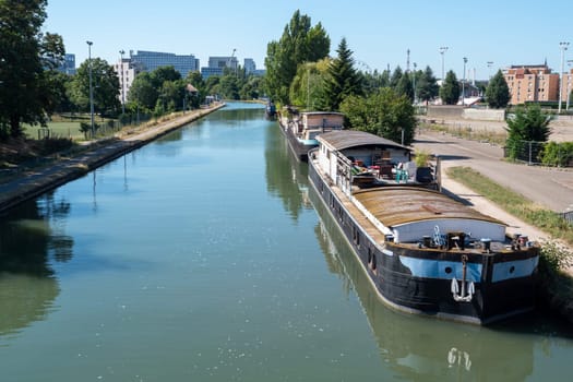 A boat is floating on a river with a city in the background. The water is calm and the sky is clear, Strasbourg, France