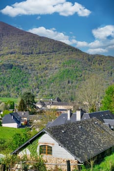 A small house with a chimney sits on a hillside. The house is surrounded by trees and the sky is blue