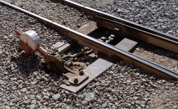 A train track with a red and white signal on the ground. The signal is missing a bolt