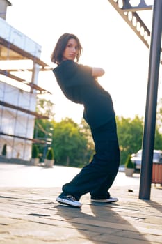 A dancer performs dynamic street dance moves in an urban environment at sunset, with a backdrop of scaffolding and soft sunlight illuminating the scene.