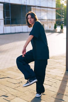 A young adult showcases a stylish pose while wearing comfortable streetwear. The urban backdrop features scaffolding, hinting at ongoing construction. It's a bright, sunny afternoon.