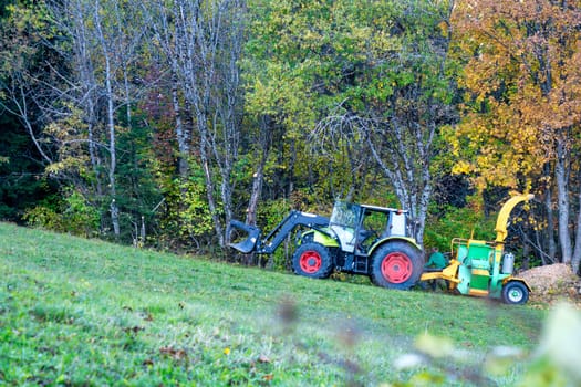 A tractor is pulling a wood chipper. The tractor is green and white