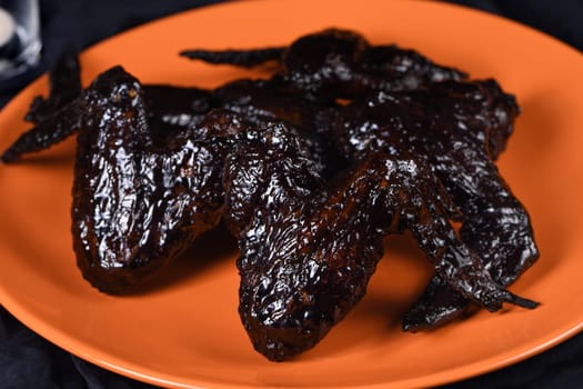 Bat wings. Cooked in sweet and sour sauce with cuttlefish ink, served with ketchup on a plate. An original idea for a Halloween party