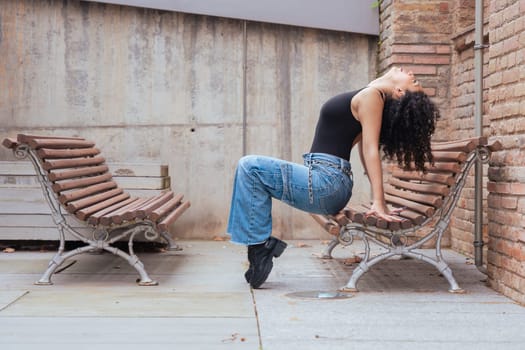 African American woman dancing in a creative pose between benches in an urban setting. She wears casual clothes and shows balance, strength, and expression. Concept of movement, art, and freedom.