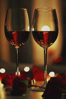 Two elegant glasses of red wine stand on a table adorned with rose petals, illuminated by soft candlelight, creating a romantic and intimate atmosphere for the evening.