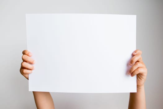 Hands holding blank white paper sheet against neutral background.