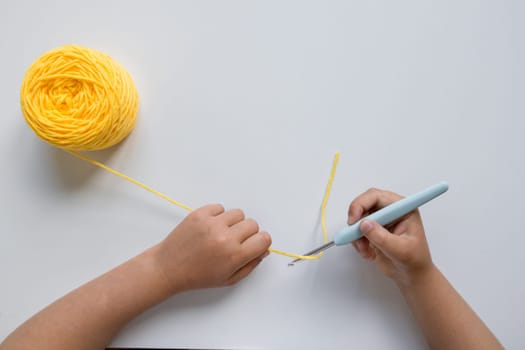 Child hands crocheting with yellow yarn on white background.
