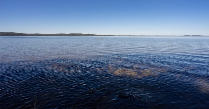 Calm lake background landscape image with blue water, blue sky, copy space for concept of serenity, peace, relaxation, calmness