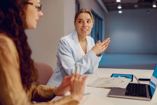 In a contemporary office environment, two skilled professional women are engaged in a discussion about ideas