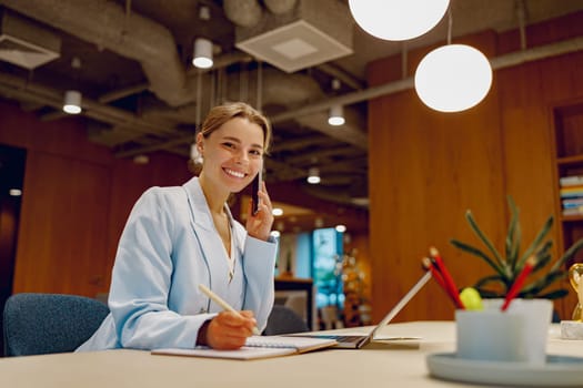 A smiling and professional woman immersed in her work at a stylish office desk featuring modern decor elements