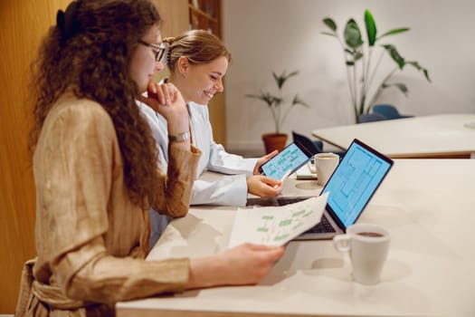 Two women are actively engaged in their work at a modern office space, carefully analyzing various data on computers