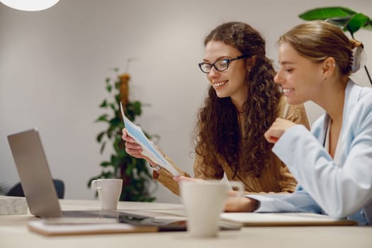 In a modern workspace, two women are actively collaborating over a laptop, epitomizing effective teamwork