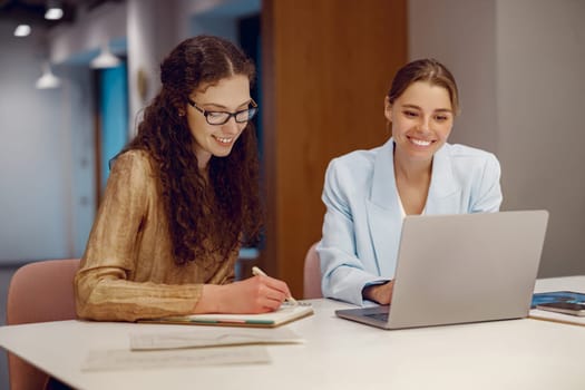 Two skilled professionals are collaborating in a sleek workspace, focusing on a laptop and their notes