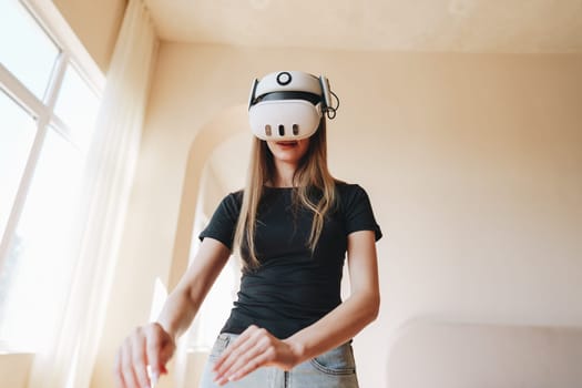A young woman wearing a virtual reality headset is fully immersed in an interactive experience. Her movements suggest engagement with her surroundings in a cozy living room setting.