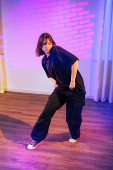 A dancer dressed in black clothing showcases contemporary moves in a vibrant urban space. Colorful lights create a dynamic atmosphere that enhances the performance.