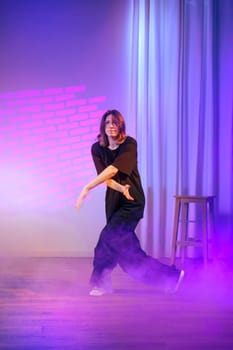 A solo dancer expresses creativity through movement on stage, surrounded by vibrant purple lights and dense fog, creating an engaging and dynamic atmosphere during a performance.