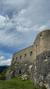 05.08.2024 Austria, Tyrol: Dramatic view of historic Kufstein Fortress wall, seamlessly built into rocky cliff. The thick stone structure with small windows blends naturally into the rugged terrain. Shot on a cloudy day, the image highlights the medieval architecture, natural textures of the rock, and the lush green grass below. Perfect for concepts of history, heritage, strength, and timeless architecture.