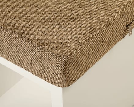 Corner detail of a removable woven fabric cover on a white storage ottoman, showing the texture and zipper