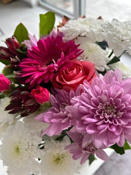 Lush arrangement of colorful blooms of pink gerbera daisies and delicate white and lila chrysanthemums with beautiful pink roses, showcasing rich pinks and whites, petals glistening with dew, surrounded by green foliage, creating a cheerful atmosphere perfect for home decor or gifting.