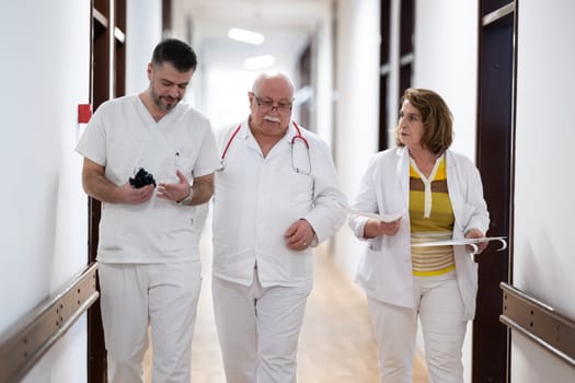 A group of healthcare professionals in white uniforms walking through a hospital hallway while reviewing patient documents and discussing treatment plans
