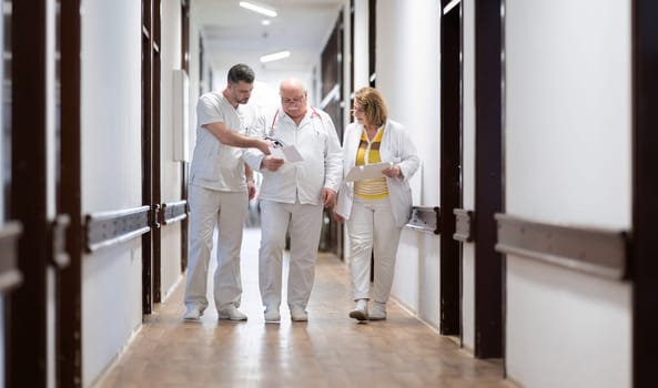 A group of healthcare professionals in white uniforms walking through a hospital hallway while reviewing patient documents and discussing treatment plans