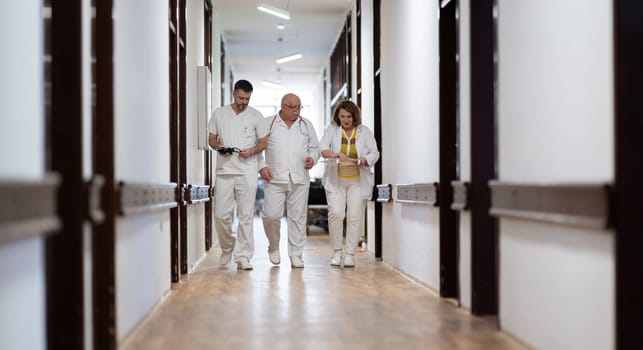 A group of healthcare professionals in white uniforms walking through a hospital hallway while reviewing patient documents and discussing treatment plans