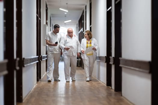 A group of healthcare professionals in white uniforms walking through a hospital hallway while reviewing patient documents and discussing treatment plans
