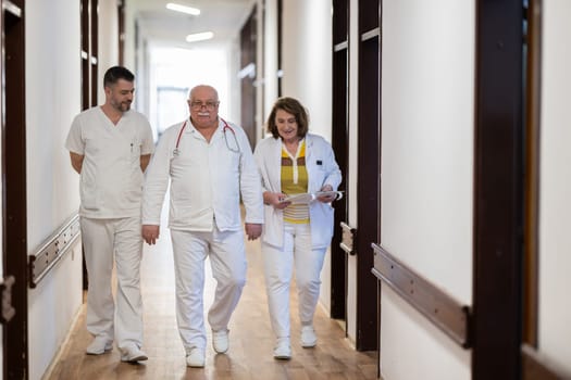 A group of healthcare professionals in white uniforms walking through a hospital hallway while reviewing patient documents and discussing treatment plans