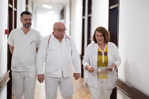 A group of healthcare professionals in white uniforms walking through a hospital hallway while reviewing patient documents and discussing treatment plans