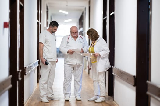 A group of healthcare professionals in white uniforms walking through a hospital hallway while reviewing patient documents and discussing treatment plans