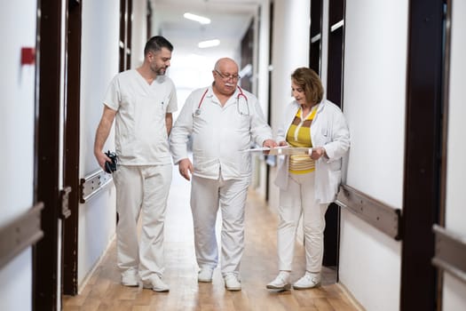 A group of healthcare professionals in white uniforms walking through a hospital hallway while reviewing patient documents and discussing treatment plans