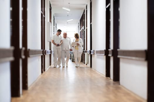 A group of healthcare professionals in white uniforms walking through a hospital hallway while reviewing patient documents and discussing treatment plans