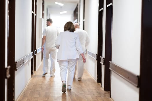 A group of healthcare professionals in white uniforms walking through a hospital hallway while reviewing patient documents and discussing treatment plans