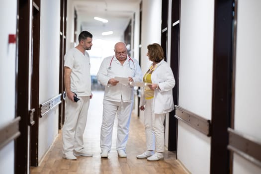 A group of healthcare professionals in white uniforms walking through a hospital hallway while reviewing patient documents and discussing treatment plans
