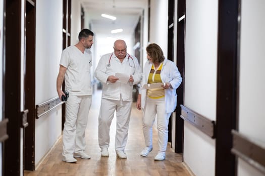 A group of healthcare professionals in white uniforms walking through a hospital hallway while reviewing patient documents and discussing treatment plans