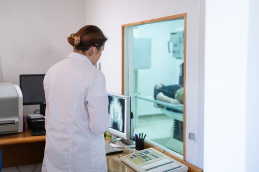 A radiologist in a white lab coat sitting at a workstation while analyzing an X-ray image of a patients hip in a medical imaging room.