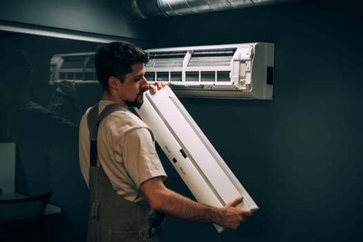 A technician carefully installs an air conditioning unit on the wall in a residential area. The process takes place indoors on a sunny afternoon, showcasing expertise and attention to detail.