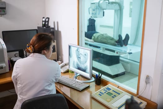 A radiologist in a white lab coat sitting at a workstation while analyzing an X-ray image of a patients hip in a medical imaging room.