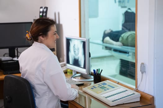 A radiologist in a white lab coat sitting at a workstation while analyzing an X-ray image of a patients hip in a medical imaging room.