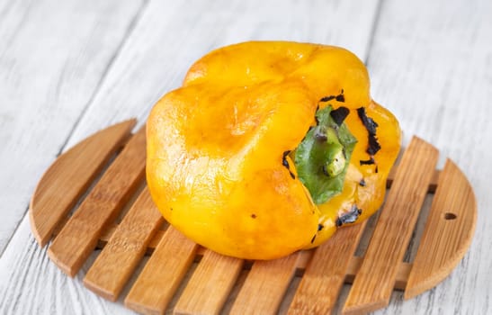 Charred yellow pepper glistens with grill marks, resting simply on aged wood