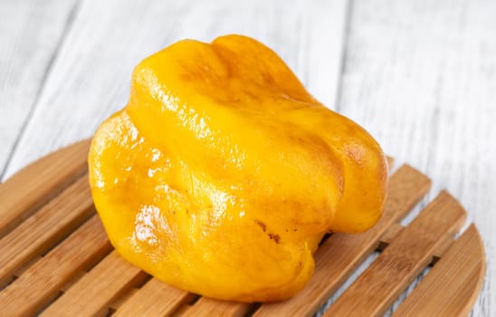 Charred yellow pepper glistens with grill marks, resting simply on aged wood