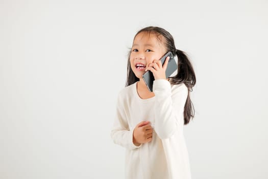 Happy Asian portrait cute young kid girl smiling excited talking smart mobile phone studio shot isolated on white background, Thai kindergarten child calling gesture on smartphone