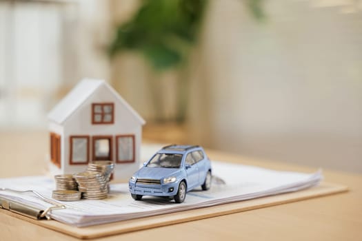 A car and house model with coins on financial documents symbolize banking, real estate savings and financial planning. Ideal for managing future goals through organized property investment strategies.