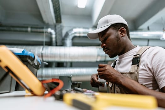 A technician focuses intently while working on electrical components in a well-equipped industrial workshop. Tools and equipment are organized on the table, indicating a detailed task at hand.