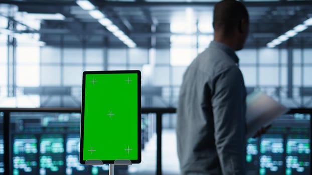 Isolated screen mockup tablet in front of technicians in blurry background working in server farm, analyzing data. Close up of chroma key tablet next to coworkers examining data center, camera B