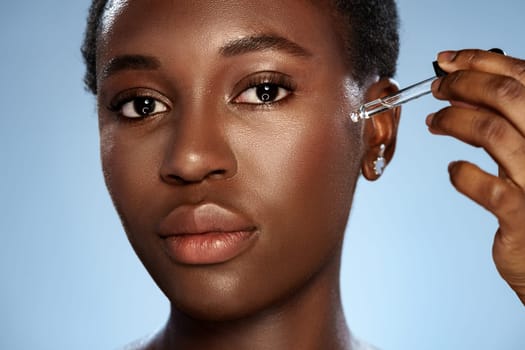 A woman applies a serum to her face using a dropper, showcasing her skincare routine. The setting is bright with a smooth backdrop enhancing her natural beauty.