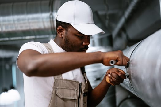 A man dressed in work attire is carefully repairing an industrial pipe.