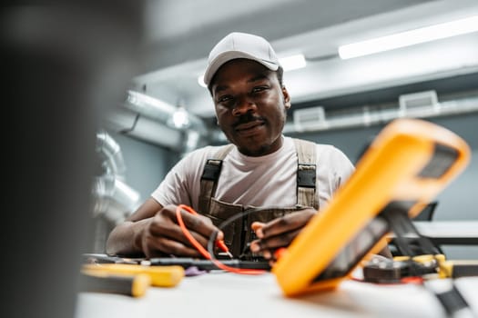 A technician is focused on repairing electrical devices at a well-equipped workshop. Tools and testing equipment are organized around him as he conducts troubleshooting.